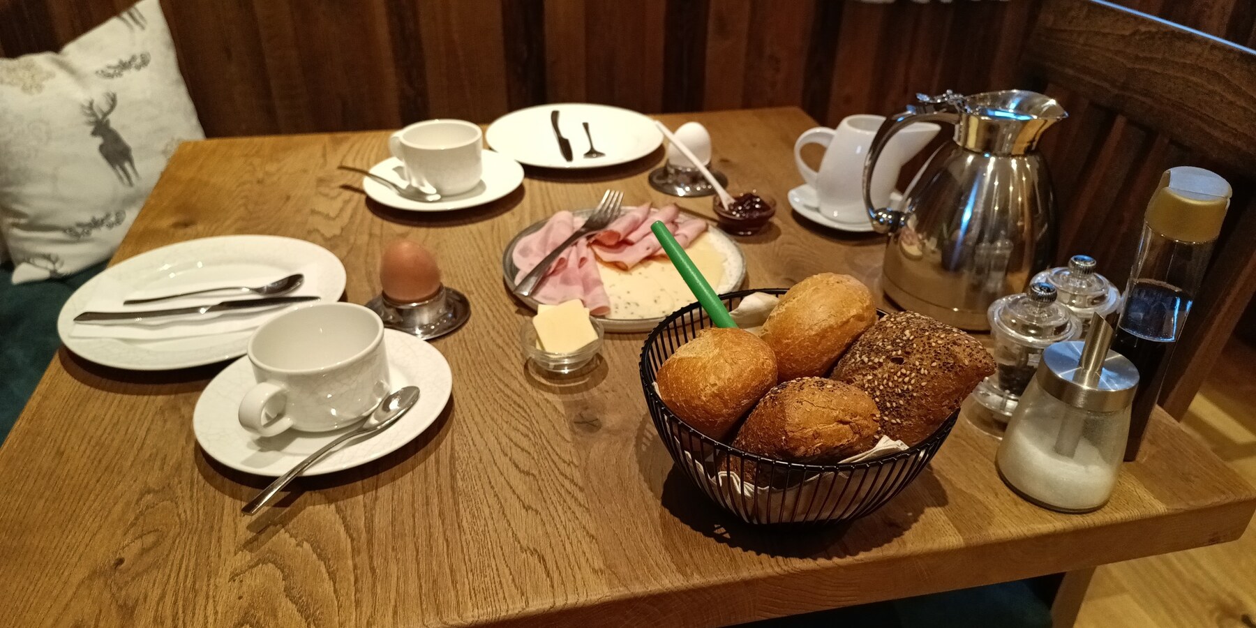 Gedeckter Frühstückstisch für zwei Personen mit Brötchen, Wurst, Käse, Ei, Marmelade, Butter und Kaffee